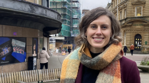 Jessica Toale has medium length brown hair and a multi-coloured scarf above a purple coat. She is stood in Bournemouth town centre.