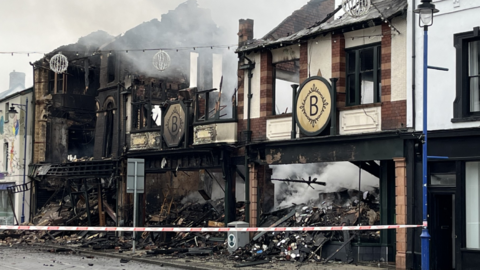 The blackened outside of the charity shop after the fire, with piles of debris and a cordon