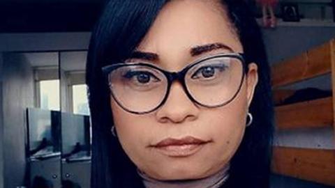 A woman with dark straight hair, black framed glasses and silver earrings 