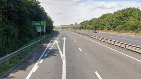 The A5, showing several lanes of traffic, with white arrows on the road, and a road sign, there are two cars on the road and a bridge in the distance. 