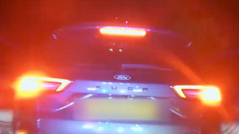The back of a purple Ford Kuga car at night with its lights on.