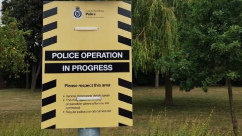 A yellow and black sign tied to a lamp post next to an area of parkland