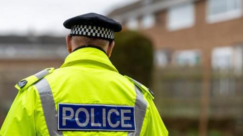 The back of a police officer wearing a high vis jacket and walking near housing