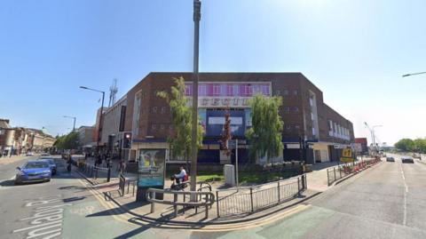 A large brown building located at the corner of a road in a city, near traffic lights. It has several small square windows and says 'CECIL' across the middle of it in bold writing beneath a long window.