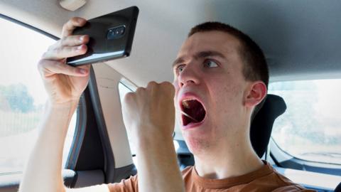 Young man using his mobile phone to help swab the inside of his mouth