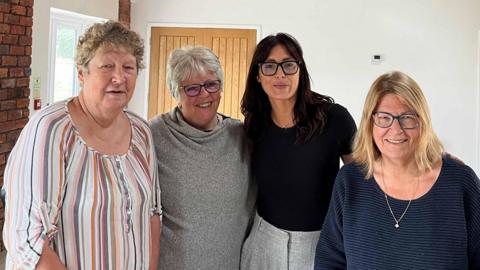 Four women - Caryl Sydney Smith, Iris Keeble, Kareen Boyd and Jo Vertannes - stood together in a newly renovated function room at the Toothill community hub. They are all looking at the camera and smiling. 