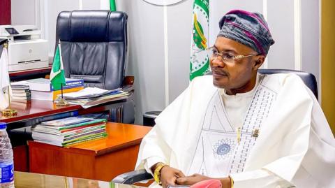 Prince Adeniyi Adeyemi Matthew, PFIPC's director general, sits in an office. He is wearing a white gown, glasses and a grey and pink cap