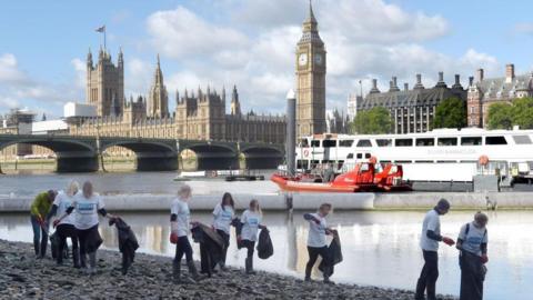 London Aquarium staff clean up bank of South Bank with Parliament behind them