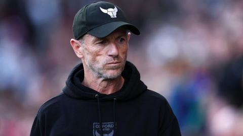 Oxford United manager Gary Rowett wearing baseball cap with Oxford bull insignia and black hoodie