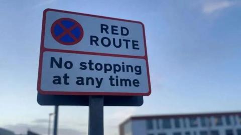 A red route sign notifying drivers that they must not stop at any time