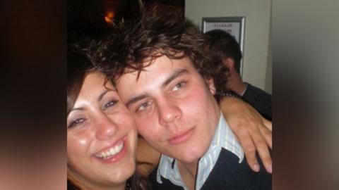 Kate Scott smiling hugging her brother Robert Chapman. He is wearing a light blue striped shirt and blue jumper.