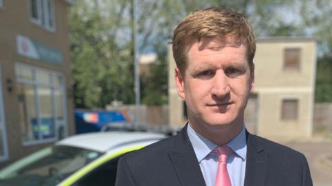 Kent Police and Crime Commissioner Matthew Scott stands in front of a police car. 