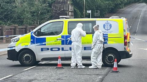 Two people in white forensic suits standing in front of a police van