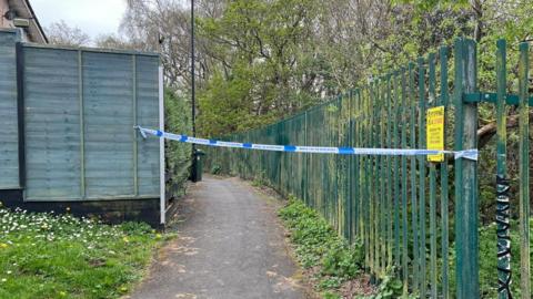 Police tape covers a path leading into woodland