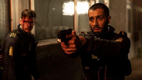 A man in a police uniform points a gun at a target off screen, another police officer stands to his left. (Image: Per Arnesen / Miso Film)
