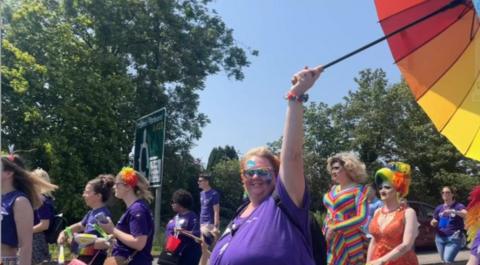 People celebrating Pride in a field, many wearing purple tee-shirts and coloured hair