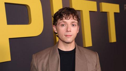 Gerran Howell, who wears a black jumper, beige suit jacket and has short brown hair