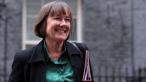 Jo Stevens in Downing Street. She is smiling, looking to the side of the camera and is holding a file under her arm. 