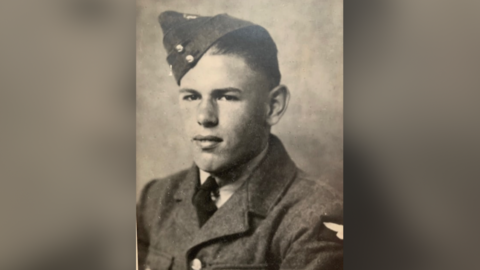 An old photograph of Alan as a young man in his uniform, which includes a thick jacket, a black tie and a pointed cap tilted to one side. 