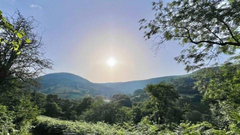 A landscape scene with the sun seen in the sky 