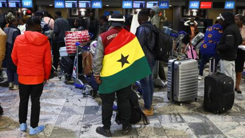 A man stands in an airport departures lounge draped in the Ghana flag