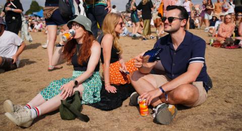 People enjoy the warm weather at the Forwards Festival at the Downs in Bristol. Two women and a man sit on the ground drinking from tins and fanning themselves.