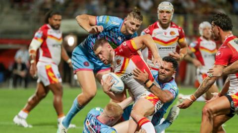 Catalans forward Bayley Sironen is tackled by Wigan duo Zach Eckersley (grounded) and Bevan French