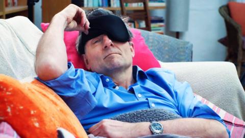 Michael Mosley wearing an eye mask while laying on the sofa
