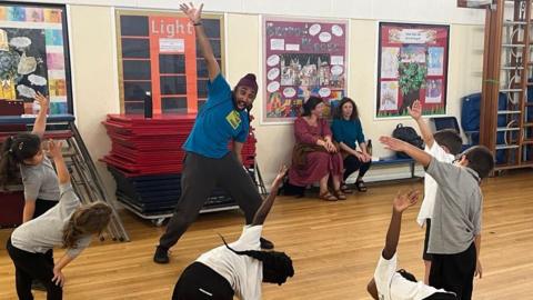 Six children dancing along with a smiling teacher showing them which moves to do