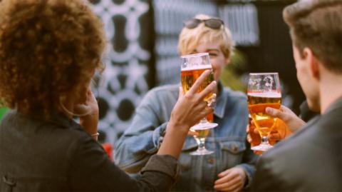 Group of young adults holding up glasses of beer to each other