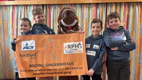 The Bolting Gingerbreads team holding a banner, with one of the students in a gingerbread suit