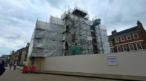 A church covered in white tarps and scaffolding on a cloudy day.