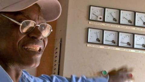 John Mwafute next to a row of dials in his power station