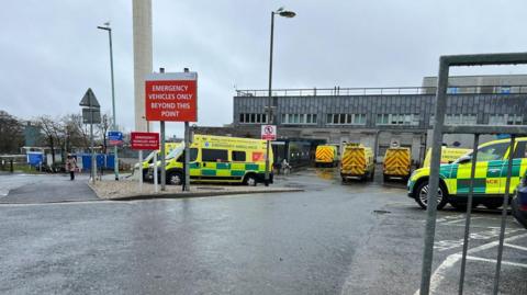 Ambulances parked outside Derriford Hospital in Plymouth on a rainy day.