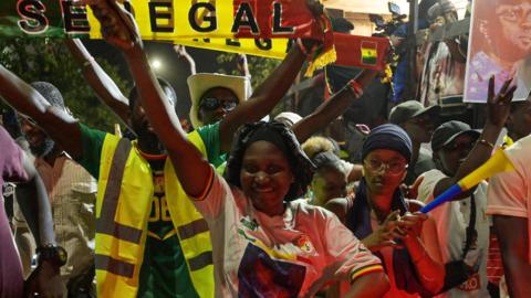 A crowd of people in an electoral campaign in Senegalese capital Dakar raising their hands and holding scarfs with the country's flag and with the words 'Senegal'
