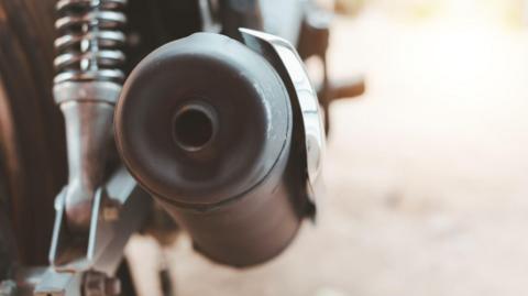 A large motorbike exhaust. The exhaust is in focus while the rest of the image is blurry.