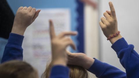 Anonymous shot of the tops of pupil's heads, sticking their hands up in a class room