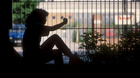 A silhouette figure of a young girl sitting behind some railings.