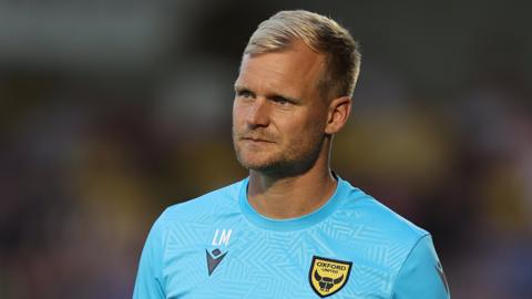 Oxford United boss Liam Manning paces up and down the touchline during a League One match.