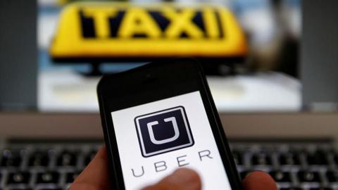 An illustration picture shows the logo of car-sharing service app Uber on a smartphone in front of a laptop displaying a yellow taxi sign 