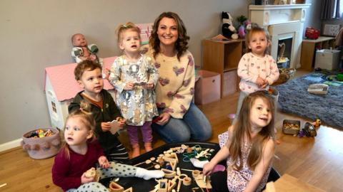 A woman with five young children and they are playing with toys