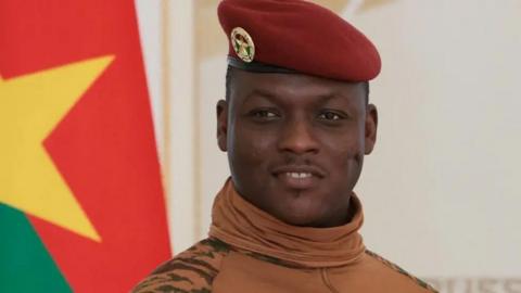 Capt Ibrahim Traoré stands next to the Burkina Faso national flag.