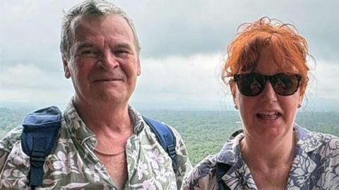 Ardon and Debbie Rainbird on holiday with a forest view behind them.