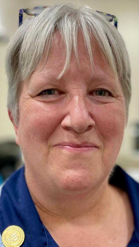 Close up of blonde woman smiling wearing a blue NHS uniform
