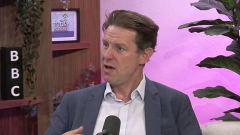 A man, Fraser Nelson, in a BBC studio - he is wearing a grey suit jacket with an unbuttoned white shirt