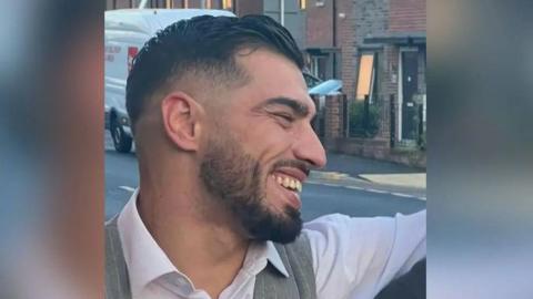 Sadiq Al-lami is seen smiling in a picture taken side-on. He is stood outside wearing a white shirt and grey waistcoat.  