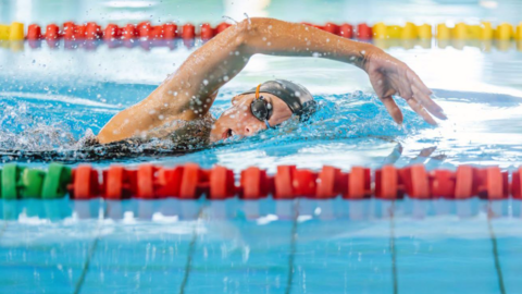 A female swimmer in a black hat and goggles is doing the front crawl.

