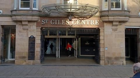 The front of the St Giles Centre in Elgin. A woman in a red coat walks through the open doors. 