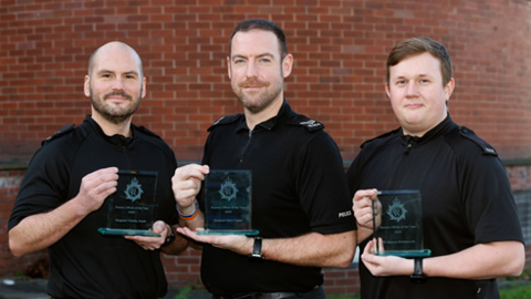 Sgt Tim Ansell, Sgt Marc Foster and PC Marcus Wolstencroft, all wearing dark police uniforms and smiling, hold up glass bravery awards with police crests on.  