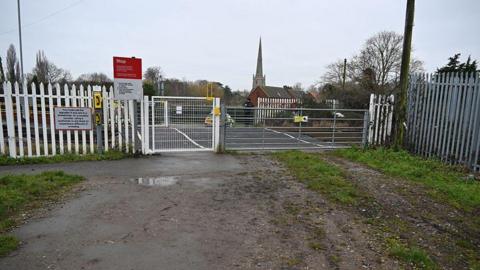 A gated level crossing with a police car parked nearby